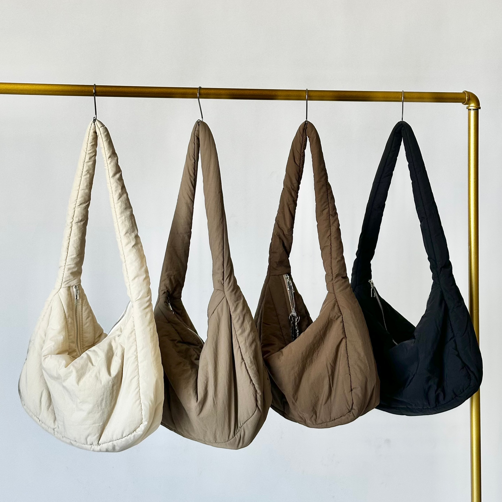 A collection of puffy plush handbags in beige, brown, and black, displayed hanging on a golden rod.